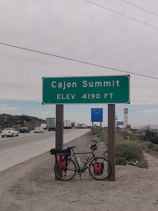 Ian's 2023 Tour  - Page 1 - Pedal Powered - PistonHeads UK - The image shows a roadside sign for Cajon Summit, indicating the elevation at 4190 feet. A bicycle is parked next to the sign, which seems to be in a desert-like environment given the dry landscape and cacti visible in the background. There's also a car parked further down the road. The sky above appears overcast, suggesting either early morning or late afternoon hours.