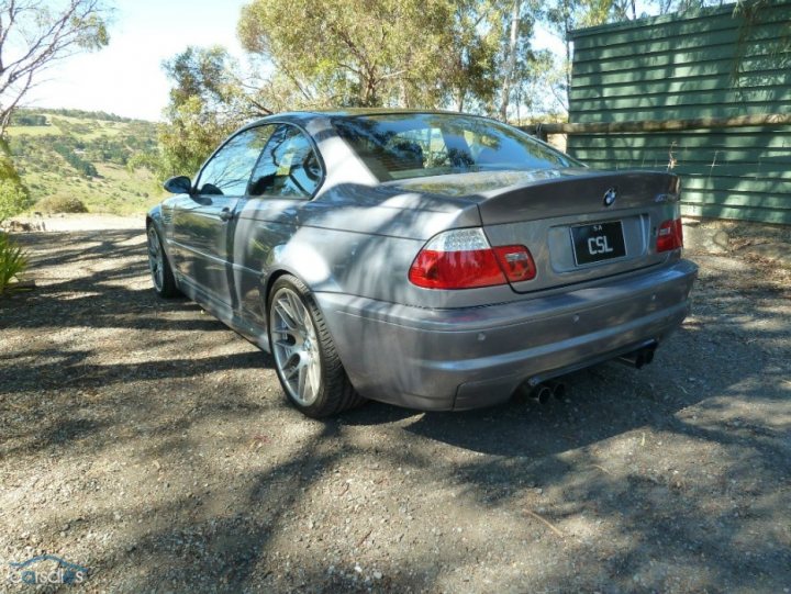 A car is parked on the side of the road - Pistonheads - The image features a silver BMW car parked on a gravel driveway. The car is positioned in profile and takes up a significant portion of the frame. The vehicle is identified by the BMW emblem visible on the trunk. The setting includes a dirt surface with patches of grass and a building and trees in the background, suggesting a rural or suburban location. The clear blue sky in the background indicates fair weather.