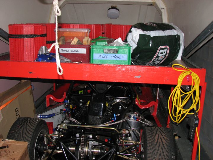 Pistonheads - This image captures the undercarriage view of a red race car. The car is equipped with multiple components including a shock absorber and a fuel tank. Tools and equipment are neatly organized in green and blue containers. Additionally, there are a few tires and yellow wires, suggesting pre-race preparations. The stunning detail of a Skulls logo beneath the car adds a dramatic touch to the scene.