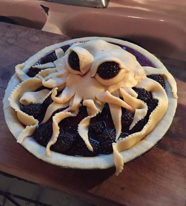 A plate of food that is on a table - The image captures a food item with a unique and creative presentation. The dish appears to be a pizza or a galette, covered with a rich, dark sauce that gives it an interesting and appetizing appearance. The unusual octopus shape on top adds a whimsical touch, making it visually appealing. The layer of fruit on the bottom suggests a sweet and savory combination. The dish sits on a wooden table, which further enhances its rustic charm.