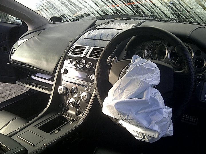 Pistonheads Warning Air Bag Stickers - The image shows the interior of a wagon or a hatchback car with a focus on the driver's seat. The center console and the vehicle's controls are partially visible, indicating a well-equipped vehicle. An unusual feature is a white, possibly crumpled, bag or baggy resting on the car's steering wheel, covering the dials. The dashboard appears to be speckled with water droplets, suggesting recent rain or condensation.