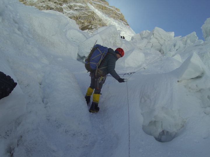 My trip to the top of Everest  - Page 11 - Holidays & Travel - PistonHeads UK - The image depicts a person hiking in an alpine setting. They are walking along a snowy path, surrounded by large snow-covered mountains on either side. The individual is equipped with a backpack and appears to be using a rope or handle, possibly for support or climbing. The scene conveys the grandeur of a mountainous environment, with the person navigating the challenging terrain.