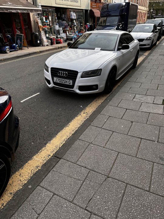 What C124PPY personalised plates have you seen? Vol.3 - Page 519 - General Gassing - PistonHeads UK - The image shows a city street scene, featuring a white Audi car parked next to the curb. The car is sleek and modern in design. It's positioned in front of a row of parked cars and has a parking meter nearby. On the sidewalk, there are various objects including handbags, backpacks, and a suitcase. In the background, there are buildings and a traffic light, indicating that this is an urban area.