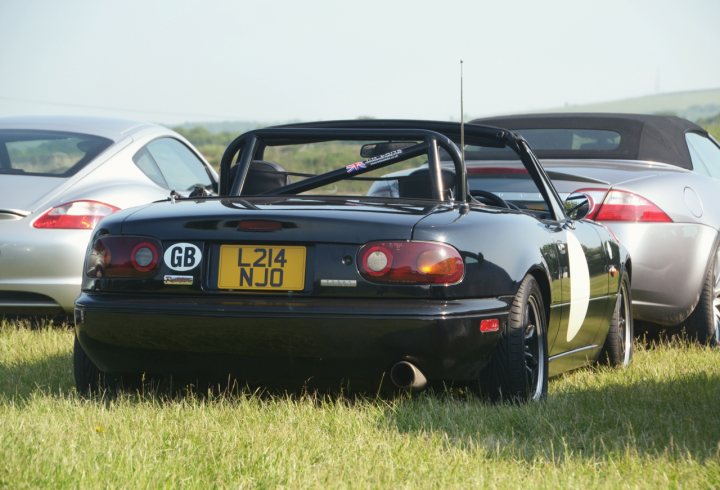 MX5 mk1 tuning - Page 4 - Mazda MX5/Eunos/Miata - PistonHeads - The image features two advanced low-drag sports cars in a field of green grass. The car in the foreground has a Austrian plate and is clearly a high-performance machine. Its bodywork appears sleek, with the roof removed to reduce drag. The car in the backdrop is partially visible, suggesting it also has similar sports car characteristics. The aesthetics of the vehicles suggest they may be part of a racing or show car event.