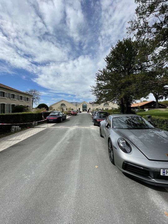 Anyone for ‘T’ - Page 194 - 911/Carrera GT - PistonHeads UK - The image is a photograph of a street scene. It shows a wide, paved road with several cars parked on the side. On the right side of the road, there's a gray sports car, and closer to the center, a silver sedan is visible. Parked further back is another gray vehicle that matches the first one in color.

There are houses or small buildings visible along both sides of the street. These structures are typically residential with a mix of architectural styles. The road itself appears well-maintained and is lined with trees, providing shade for the parked cars. The sky above suggests it's a clear day with ample sunlight.

In the background, there is a building with a sign that reads "CHURCH" in English, indicating the presence of religious infrastructure nearby. Additionally, there are a few cars parked along this stretch of road as well. The overall setting appears to be an urban or suburban residential area.