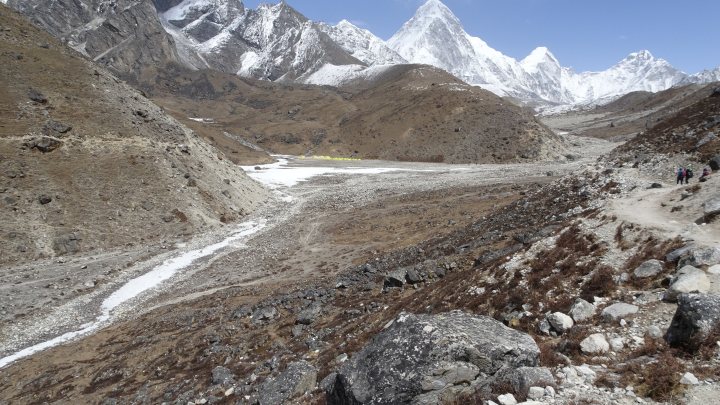 My trip to the top of Everest  - Page 8 - Holidays & Travel - PistonHeads UK - The image depicts a rugged, mountainous landscape. Dominating the foreground is a vast expanse of snow-capped mountains, their peaks stretching towards the sky. In the midst of these towering formations lies a valley, where a dirt road meanders through the terrain, leading the eye towards an unseen destination. The ground is strewn with rocks and scattered vegetation, adding to the ruggedness of the scene. The sky above is clear, suggesting good weather conditions. The image captures the raw beauty of nature in all its untamed glory.