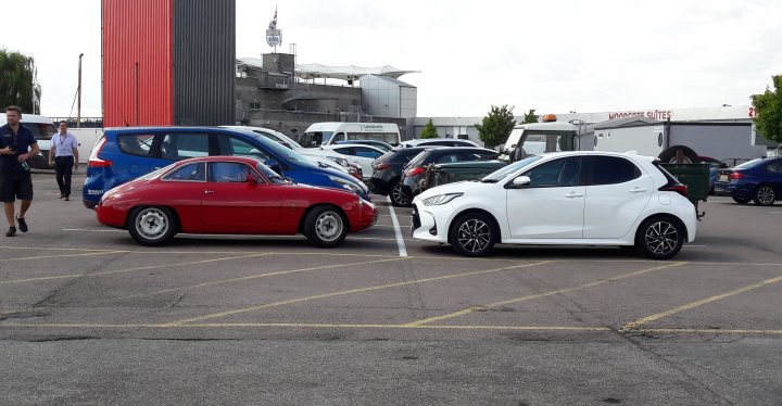 Classics dwarfed by moderns - Page 131 - Classic Cars and Yesterday's Heroes - PistonHeads UK - The image is a split-screen photograph showing two different scenes. On the left side, there's a scene in what appears to be a parking lot with several cars parked and people standing around. A few individuals are visible, but their activities are not clear. On the right side, there's another scene with a row of parked vehicles, including a red sports car that stands out due to its bright color. The backdrop of this scene includes a building with the word "Sport" written on it, suggesting it might be related to automotive events or activities.

The contrast between the two scenes is striking, with the left side depicting an everyday urban setting and the right side possibly indicating a special event or location dedicated to sports cars. The image does not contain any text or distinctive logos that could provide additional context about the specific locations or times these images were taken. The style of the image suggests it might be used for a comparison between different environments or events, possibly related to sports cars.