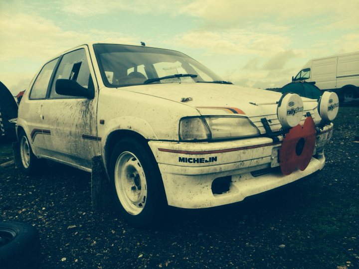 Stage Rallying - the costs? - Page 1 - UK Club Motorsport - PistonHeads - The image depicts a rusted out white hatchback parked on a gravel surface. The car has some elements of modifications with a spoiler mounted on top and aftermarket tail lights. There's noticeable corrosion on the body, ground clearance, and undercarriage, indicating a condition that has likely been exposed to harsh environments or left unused for an extended period.