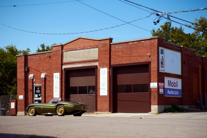 1967 Ferguson SuperSport - Page 1 - Classic Cars and Yesterday's Heroes - PistonHeads UK - The image presents a scene at an old, abandoned fire station. Dominating the foreground is an antique car parked in front of the building. The car's vibrant yellow color contrasts with the aged red brick exterior of the fire station. In the background, power lines and trees can be seen, adding to the overall atmosphere of the scene. The sky above is clear and blue, suggesting a pleasant day.