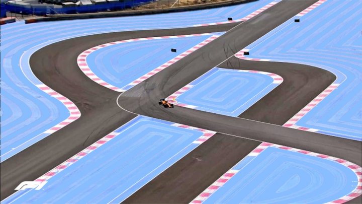 Official 2021 French Grand Prix Thread ***SPOILERS*** - Page 5 - Formula 1 - PistonHeads UK - The image is a photograph of a motorsport race track, likely used for drag racing or similar high-speed events. The track has multiple lanes and curves, with each lane marked by white and blue lines that suggest the direction of travel for vehicles. There's a single vehicle on the track, captured in motion as it appears to be in the initial stages of acceleration. The surroundings include what looks like an advertising banner or billboard to the right side of the image. The background is mostly clear, emphasizing the racetrack.