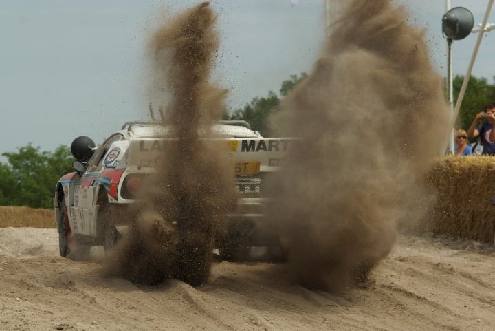 FOS good photography vantage points.. - Page 1 - Goodwood Events - PistonHeads - The image depicts an intense moment during a motorsport event. A dirt racing car is driving away from the viewer along a dirt track, kicking up a significant amount of dust and debris in its wake. The car appears to be in motion, possibly speeding down a steep incline or ramp. The background shows spectators, indicating the car is performing in front of an audience, adding to the excitement and competitiveness of the scene. The image captures the dynamic nature of the sport and the thrill of the race.