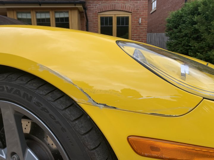 What should I do regarding this damage? - Page 1 - Bodywork & Detailing - PistonHeads UK - The image shows the front end of a yellow sports car. There is visible damage on the hood, which suggests it has been involved in an accident. The car's headlight and grille are intact, while the bodywork around the hood area is damaged. The vehicle is parked outdoors in front of a residential house with brick walls and a white door frame.