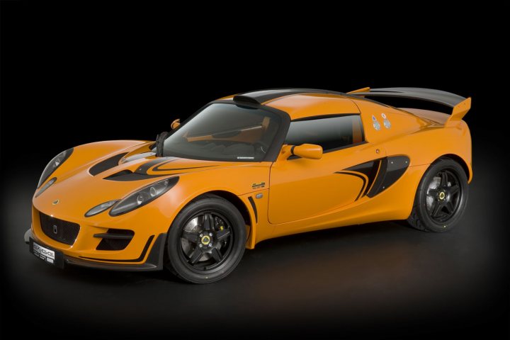 Forged alloys - Page 1 - Elise/Exige/Europa/340R - PistonHeads - The image shows an orange racing car against a black background. The vehicle has two doors and a rear wing, giving it a sleek, aerodynamic design. Its wheels are black with yellow accents, matching the citrus color of the car. The car appears to be a toy or a model, given the low angle and the way it is stylized. There are no visible texts or branding in the image.