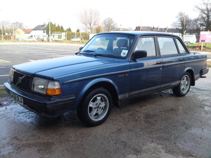 Collectable Volvo Pistonheads Gle - The image captures a compact blue car parked on a wet surface in what appears to be an outdoor parking lot. The vehicle is facing the camera and has a German license plate. There are no visible people in the image. The car's condition and the puddle on the ground suggest it has been raining recently.