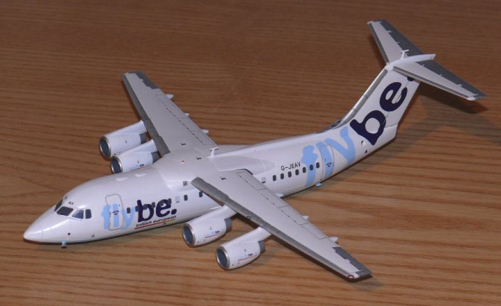 Pistonheads Avro Revell Bae Flybe - The image features a white, three-function, propeller airplane model which is resting on a wooden table. The aircraft has a large body with wings stretching out on either side, each equipped with two propellers. The tail of the plane has a blue and white logo with the word "be." The plane is designed with the overall shape, size, and layout typical of small commercial aircraft. The model may be a product of the Britten-Norman company, as indicated by the lettering "G-IML" on the exterior of the aircraft. The overall scene is realistic and detailed, but it is an inanimate model and does not depict a real, moving aircraft.