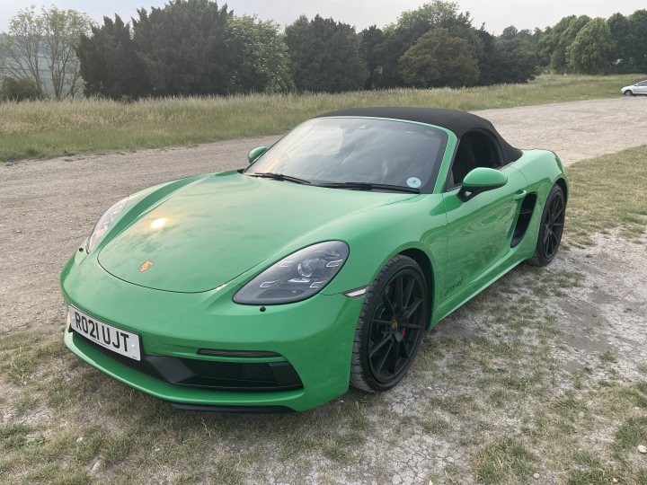 A picture a day... Porsche - Page 213 - Porsche General - PistonHeads UK - The image shows a vibrant green Porsche sports car parked on an asphalt surface. The vehicle has distinctive design features, such as the wide-body kit and large rear spoiler. There's a license plate on the back of the car that reads "J71 JGK." The surroundings suggest a rural area with grassy fields in the background. The sky is overcast, indicating cloudy weather conditions.