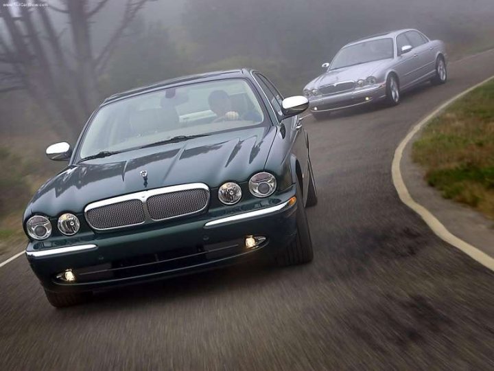 Jaguar Thoroughbred Pistonheads Saloon Nicest - The image captures the scene of a rural road being shared by two cars. One car is a bright blue convertible positioned in the foreground, while the other is a metallic gray sedan. The cars are in motion, driving on the right side of the road, with the blue convertible being slightly ahead of the gray sedan. The road itself is a two-lane asphalt path, bordered by grass and trees, creating a serene and picturesque setting. The sky above is overcast, adding a dramatic touch to the overall scene.