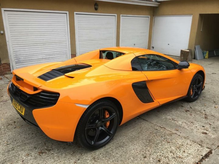 Happy Day - New 650S Spider - Page 1 - McLaren - PistonHeads - In the image, parked on the driveway of a home is a gleaming orange sports car. The car has its top down, revealing a sleek interior. Its bodywork is well-maintained, with distinctive black and orange accents adding to its sporty appeal. Behind the car, there's a quiet residential setting with a garage visible.