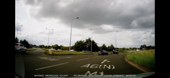 Write Off? - Page 1 - Bodywork & Detailing - PistonHeads - The image appears to be a screenshot from a video recording, as indicated by the play button icon at the top of the frame. It shows an outdoor scene with a road stretching into the distance under a gray, cloudy sky. There are several vehicles on the road, including cars and trucks. On the left side of the image, there's a street sign, although its text is not clearly legible. The overall quality of the image suggests it may have been taken from a security or traffic monitoring camera.