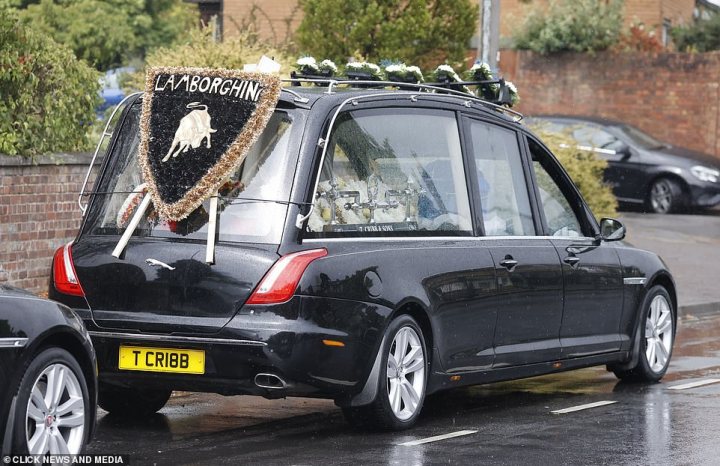 What C124PPY personalised plates have you seen? V01. 3 - Page 401 - General Gassing - PistonHeads UK - The image shows a black car parked on the side of a road. On top of the car, there's a large flower arrangement, possibly indicating a funeral procession. A plaque on the car reads "Caledonia" which might be the name of the funeral home or the funeral itself. The vehicle is adorned with a sign that seems to say something about "Crooked" and a phone number, but it's not entirely clear. In the background, there are some trees and what appears to be a street lamp or light pole. There's also an animal statue near the car, possibly serving as a decorative feature for the funeral procession. The overall setting suggests a solemn event is taking place.