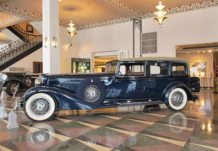 Car stuff worth seeing in the northern US & canada? - Page 1 - USA & Canada - PistonHeads - The image features a striking vintage car, prominently displayed on a checkered floor of a room. The car, painted in a dark color, highlights the iconic design of its era. It is a classic station wagon, enhancing the sense of nostalgia and time travel within the room. Positioned on the spacious floor, devoid of any other vehicles or obstructions, the car is displayed in a garage-like setting, adding to the overall vintage ambiance. The setting appears to be well-lit, likely with spotlights hidden from view, which further accentuates the car and its detailed features.