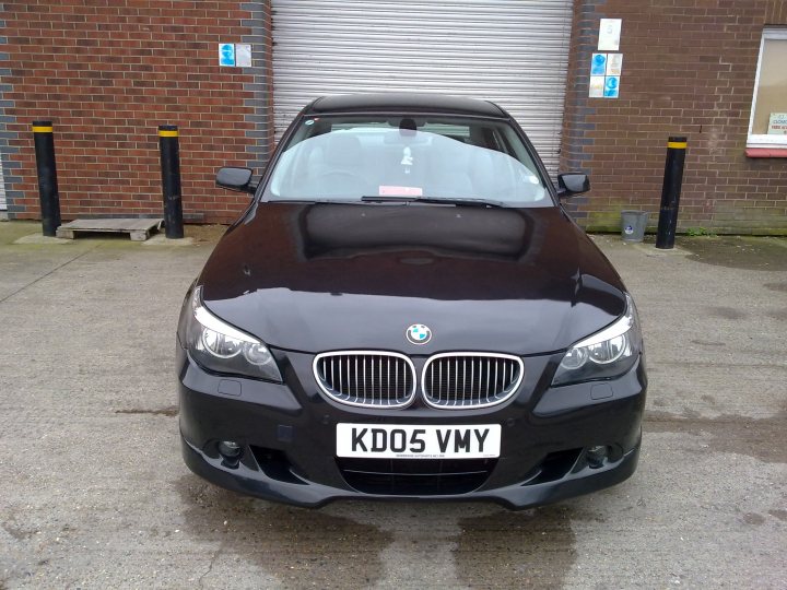 Pistonheads Bmw Kevin - This image shows a black BMW car parked on what appears to be a street or lot. The car is oriented to the left side of the image, as seen from the driver's perspective. The vehicle is parked in a covered space, with a closed weatherproof section over part of the car. In the background, there's a brick building with closed doors to the left of the car. To the right of the car, there's an open doorway, and on the right side of the image, a gate is partially visible.