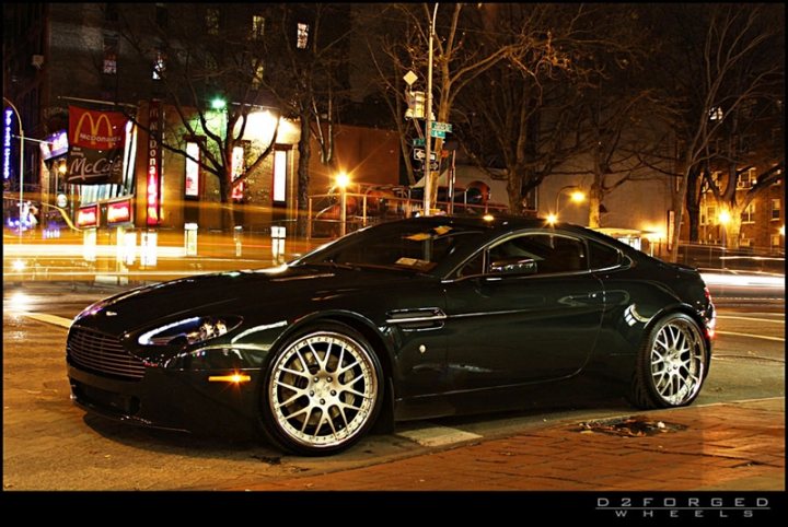 Car Porn - Page 1 - Aston Martin - PistonHeads - The image features a sleek black sports car parked at night on a city street. The vehicle is a standout, with its doors and hood both open, as if inviting a closer look. The surrounding area is quiet, with illuminated street lights softly reflecting off the wet pavement due to recent rain. The scene captures the tranquility of the urban landscape at night, with the glowing car as the focal point.