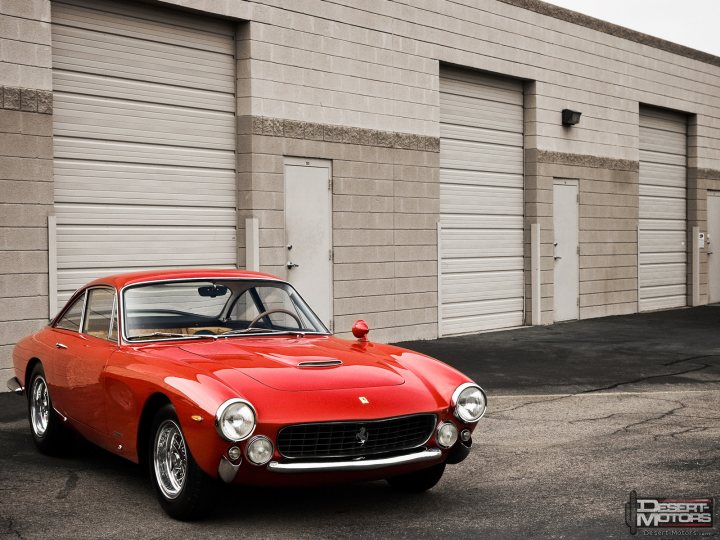 Pistonheads Prettiest - The image features a striking red Porsche 911 Turbo S parked in a garage. The garage doors in the background are closed, suggesting a secure and sheltered environment. The car exhibits a classic sloped rear windshield, indicative of the Porsche 911 model's design, and the overall style and presentation of the image give it a vintage or retro feel. The composition of the image, with the car centered and the garage doors providing a backdrop, draws attention to the car and its vibrant red color.