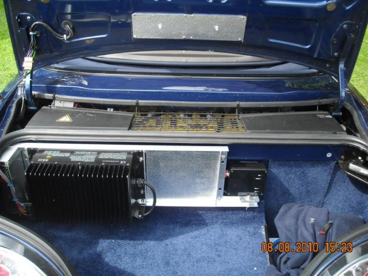 Pistonheads - The image provides an interior view into a vehicle's trunk. A black exhaust system can be seen along with what appears to be the space where the battery is typically located. There is a stereo system installed, visible beneath a protective black cover. The vehicle seems to be a compact or subcompact car, given the size of the trunk compartment. The trunk lining is blue, offering a contrasting detail in the image. There isn't any additional context or visible objects that other than the car parts, require attention. The image does not provide enough information to discern the make or model of the vehicle.