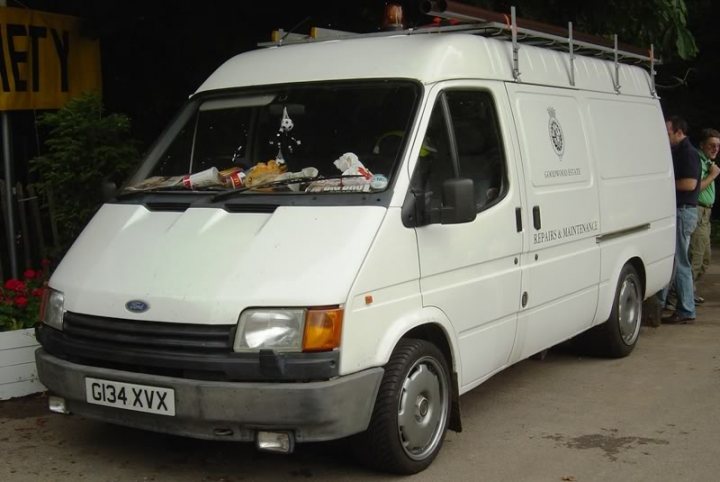 Cars that go better than they look! - Page 1 - General Gassing - PistonHeads - The image showcases a large, white commercial van parked on a street, adjacent to a yellow sign that reads "SAFETY." The vehicle appears to be a work van, as suggested by the safety sign. The van is equipped with a rack on top, indicating it may be used for transporting goods or equipment. There are various items on top of the van, including what seems to be a crate of goods. In the background, there are two individuals, but details about them are unclear.