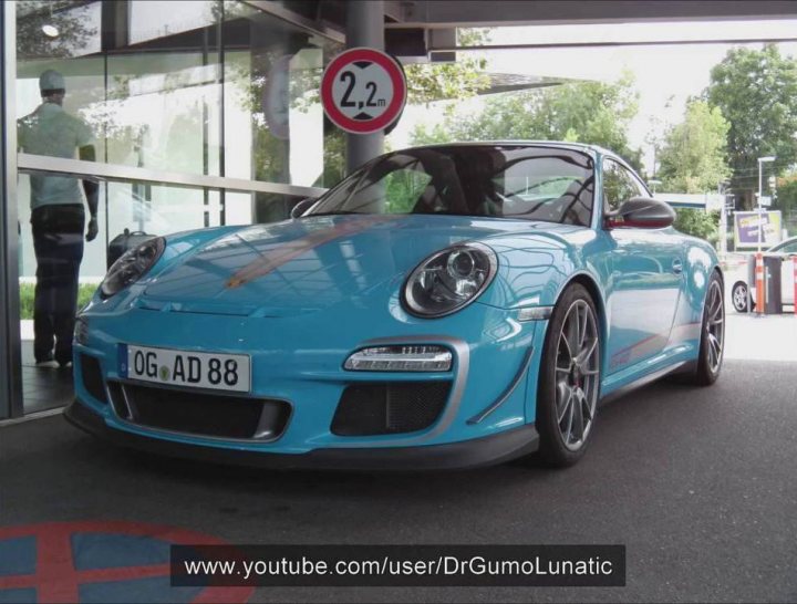 RS 4.0 values  - Page 13 - 911/Carrera GT - PistonHeads - This image presents a captivating scene of a blue Porsche 911 GT2 RS car parked under a covered area. The car, with its shiny blue exterior, dominates the foreground of the photograph. The positioning suggests it's parked next to a large glass window that likely serves as a salon window for the building next to the garage. In the background, there's a sign with a '2' symbol and the number '223' which might indicate an entrance or lane number at a parking facility.