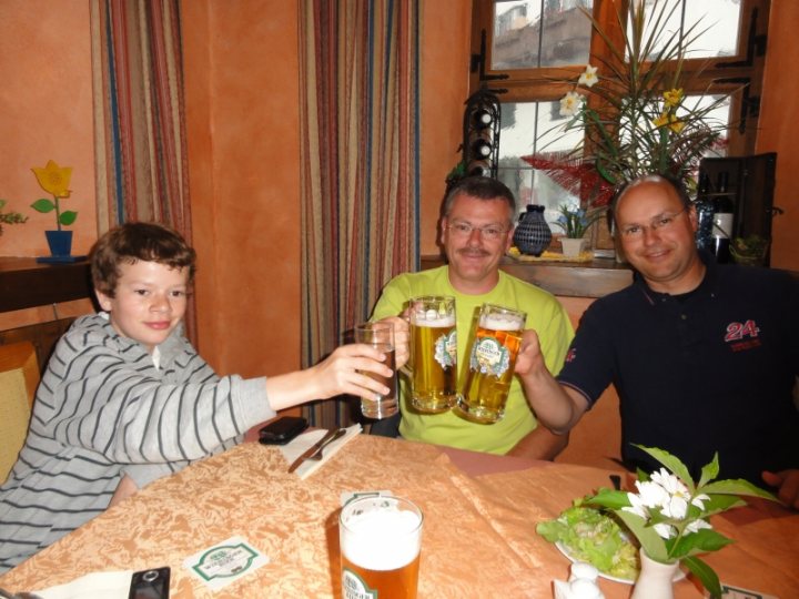 Celebrating 20 years of ... - Page 1 - Vipers - PistonHeads - The image depicts a serene setting of three individuals sharing a moment of joy around a dining table. One person is seated in the foreground, lightly touching a frosted mug filled with beer. The other two individuals stand behind him, their faces lit up with smiles as they lift their own frosted mugs in a toast. The table is set with a variety of items, including a plate, vase, and a wine glass, suggesting a casual and warm gathering.