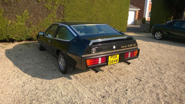 1981 Lotus Eclat 2.2 - Page 1 - Readers' Cars - PistonHeads - The image captures a serene scene in a gravel driveway. On the left, an older, black model car stands on its own. It's a classic, reminiscent perhaps of the 1980s, with a license plate that reads "PUA 534". The vehicle's nostalgic design contrasts with the pristine gravel surface. In the background, a brick house with a white door can be seen, adding a homely touch to the scene. The gravel driveway leads up to the house, creating an inviting path.