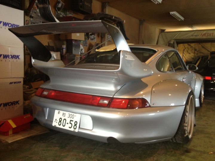 RWB Porsche for Sale - Nakkai San's car  - Page 1 - Middle East - PistonHeads - This image features a sleek, metallic-colored Porsche, parked inside a well-lit garage. The car's distinctive tail is prominently visible, adorned with a spoiler and the iconic round Porsche lights. It's surrounded by packaging materials and other objects, suggesting it's either been recently purchased or prepared for an event. The garage has a workshop-like vibe, with various tools and equipment indicating that it's a space for automotive work and maintenance. The overall atmosphere is one of cleanliness and professionalism, likely where enthusiasts keep and care for their prized possessions.