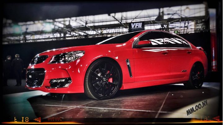 A red car is parked on the side of the road - Pistonheads - The image captures a vibrant scene featuring a striking red sports car. The car is parked indoors, likely at a car show or exhibition, as indicated by the presence of a person in the frame, possibly a car show attendee. A large VFI sign is displayed in the middle ground, suggesting some form of automotive event or sponsorship. The red hue of the car dominates the image, its glossy finish reflecting the overhead lights. The car's position on a raised platform draws attention to its unique features, emphasizing its status as a prized vehicle.