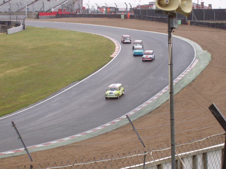 BRSCC Meeting Brands Hatch 11-06-2011 - Page 1 - UK Club Motorsport - PistonHeads - The image depicts an action-packed scene on a race track. Several cars are streaking by at high speed, their movement creating a sense of motion and excitement. The perspective is from the stands above the track, giving a panoramic view of the race.

The track itself is a vibrant and curved lay of tarmac, guiding the rapid direction changes of the cars. The infield of the track is an expanse of sandy dirt, contrasting with the smooth, dark track surface.

The day looks overcast, with a grey sky stretching across the tops of the monitor. The cars are evenly spread out across the track, suggesting that this is a race or competitive event. The speed and positioning of the cars give an impression of a spirited race in progress.