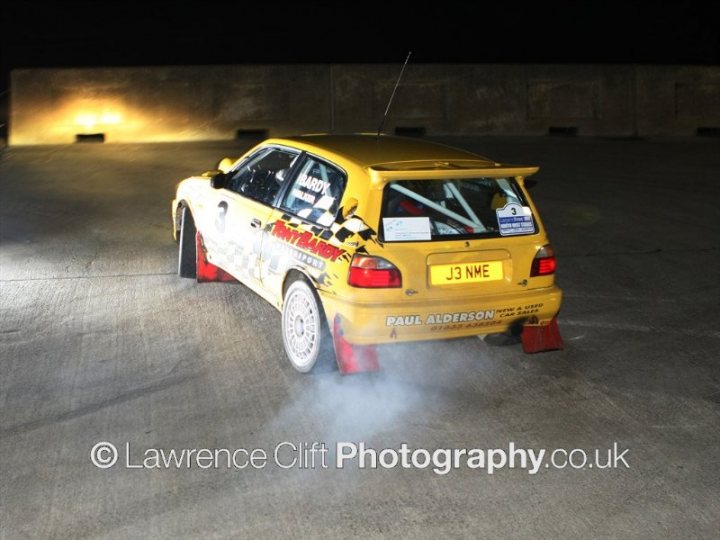 Pistonheads - The image showcases a modified yellow and black Volkswagen Golf GTI parked sideways on a deserted highway. The car is adorned by numerous stickers, distinctive aerodynamic modifications, and brake discs, some with a blue and white pattern. Its license plate tips off the car's name as "Rally Jim". Surviving the scene is a disco ball, seemingly unbothered.