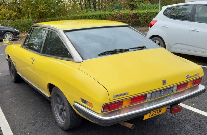 A red car is parked on the side of the road - The image shows a classic yellow sports car parked in a parking lot. The vehicle is positioned facing left, with the front end visible and its sleek design indicative of the 1960s or 1970s. The car appears to be well-maintained, suggesting it might still be in use or used for special occasions. In the background, there are trees and a building, typical of an outdoor setting, but the focus remains on the yellow sports car. There's also a license plate visible on the vehicle, which adds to the authenticity of the scene.