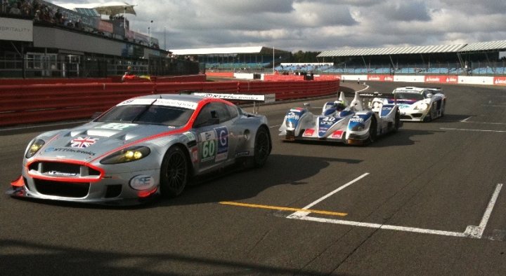 Sept Silverstone Pistonheads Series - The image captures a thrilling moment in a race where multiple race cars are driving on a track. The cars are predominantly silver and blue, with the front car's chrome front and red number seven adding a striking contrast. In the background, you can see grey and white buildings, possibly part of a larger racing facility. The sky overhead is full of clouds, suggesting that the race is taking place under somewhat overcast conditions. The overall scene is a dynamic display of speed and technology.