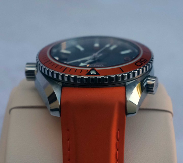 Pistonheads - The image shows a watch on a display stand. The watch is predominantly orange and black with a red strap, featuring a round case and what appears to be a chronograph function indicated by three smaller dials around the main dial. There's a visible date window between 4 and 5 o'clock positions. The brand name and model number are printed on the watch face, but I cannot describe them without potentially identifying the brand. The background is neutral and does not distract from the watch itself. The style of the image suggests it may be for promotional or sales purposes, given its presentation on a display stand.