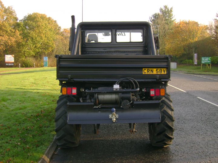 Legal Off Road Modifications - Page 1 - Off Road - PistonHeads - The image shows a large black off-road vehicle, possibly a tractor or a commercial vehicle, predominantly painted in the color black. It's parked on the side of a road with what appears to be a light reflective tape, indicative of a white strip painted on the pavement, marking part of the road. In the background, the natural landscape is visible with a few trees and yellow grass, which suggests a park or a rural area. Additionally, there's a road sign that displays directional information, but the text is not legible in the image. The vehicle seems to be well-maintained, as indicated by its shiny bodywork and the absence of visible damage or wear.