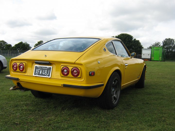 Datsun 240 or 260Z - Page 1 - Classic Cars and Yesterday's Heroes - PistonHeads - The image shows a vibrant yellow MG (Morris Garages) sports car parked in a grassy field. The car's license plate is clearly visible and reads "CA 4Y 386". The car's headlights and tail lights are red. In the background, there are other vehicles partially visible, including a bright green van. The sky behind the field is slightly cloudy.