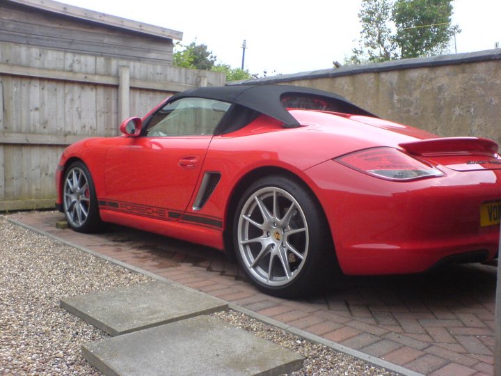 That rear wiper... - Page 1 - Boxster/Cayman - PistonHeads - The image features a vibrant red convertible sports car parked in a driveway. The car is positioned in such a way that the front is facing the camera, displaying its striking color and sleek design. The car's soft top roof is closed, indicating it is currently a coupe. The driveway itself is paved with cobblestones, adding a touch of elegance to the scene. The wall in the background is composed of wooden paneling, providing a contrast to the brick driveway and the red car.