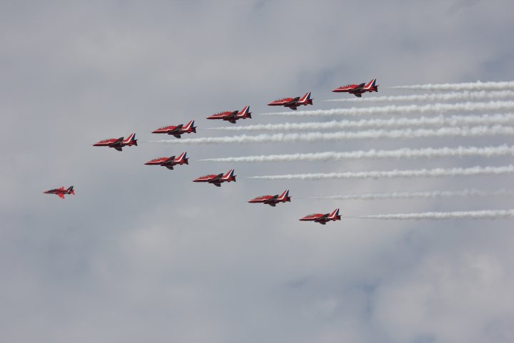 A group of planes flying in the sky - Pistonheads - The image captures a breathtaking sight of nine jets performing a precision flyover. The jets are painted in a striking combination of red and white and are flying in a tight formation. The sky, filled with light gray clouds, sets a dramatic backdrop for the aerial spectacle. The trailing contrails from the jets add to the visual effect, leaving behind a pattern of white lines in the sky. The image is a dynamic display of aerial acrobatics, showcasing the precision and skill of the pilots.