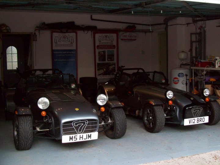 Hot Pistonheads Leg Sigma - In the image, there are three vintage sports cars parked in a garage with a high ceiling. One car is black, another is silver, and the third is gray. The garage has visible pipes and a workbench to one side. The license plates of the vehicles read "V52 BRO", "M5 HJM", and "V52 BRO", suggesting they could be related or owned by the same person. The overall atmosphere of the image is one of nostalgia and passion for classic vehicles.