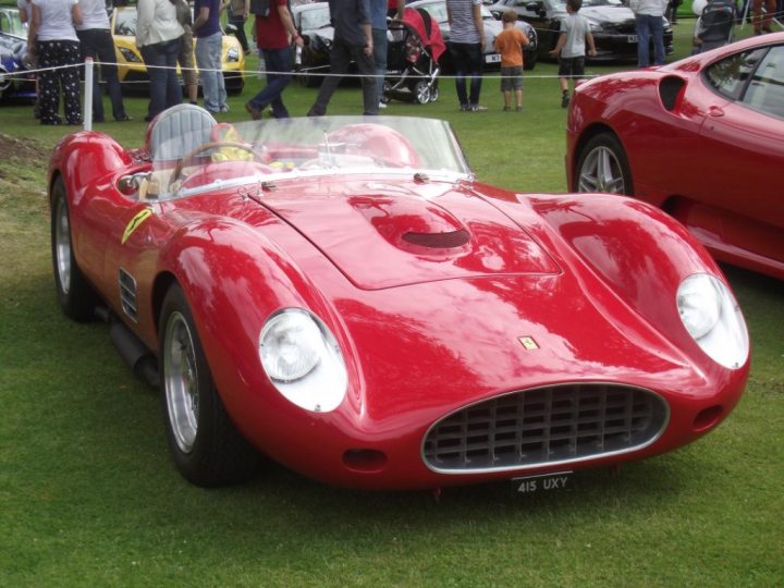 Wilton House - Page 1 - South Wales - PistonHeads - This is a vibrant image featuring a red, vintage racing car on display on a green grass field. The car has a sleek design, with sharp angles and curves that hint at its speed and performance. It's a Ferrari, as indicated by the logo and emblem on the side. Surrounding the car, you can see a crowd of people admiring the vehicle and the classic design of the median strip of the race car rearview mirror. The background is filled with other classic cars parked in neat rows, adding to the captivating atmosphere of the automotive event.