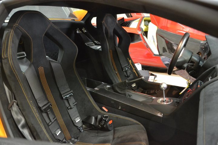 A pile of luggage sitting next to each other - Pistonheads - The image captures the interior of a sleek sports car, showcasing what appears to be the passenger side's driver seat. The car's interior is predominantly black, with leather seats featuring gold accent lines. The seat is adorned with a striking orange design, adding a pop of color to the space. The perspective of the image is particularly interesting as the car's steering wheel is visible, suggesting the viewer may be seated behind the wheel. This placement provides a unique first-person view of a luxury sports vehicle's cabin.