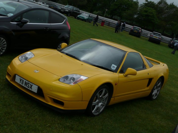 Stunning Nsx Yellow Pistonheads - The image depicts a vibrant yellow sports car parked on a grassy field. In the background, there are several other cars, indicating that this might be a car show or a gathering of enthusiasts. The sports car features the Honda NSX model name and is facing towards the viewer. The field is lush green, suggesting it might be spring or summer. The car's sleek design and bright color make it stand out against the natural backdrop.