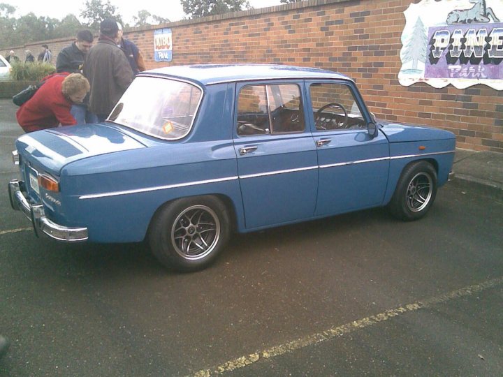 Renault Add Pistonheads - The image showcases a vintage car, painted in a vibrant shade of blue. It's parked in a parking lot, surrounded by other cars. The car, with its white roof and chrome rear bumper, exudes an old-world charm. The sight attracts onlookers, as visible from the gathering of individuals near the car. The car's make is hinted at by a visible sign in front of it, suggesting it could be a preferred car model or brand.