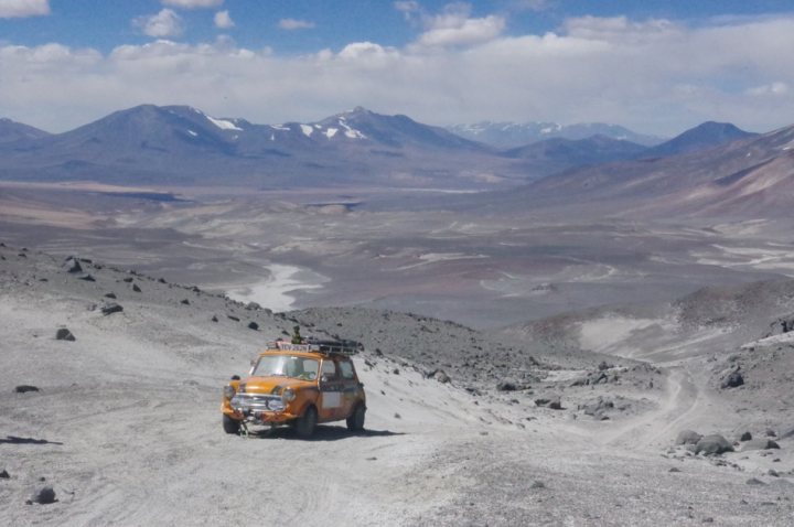 Pistonheads - The image depicts a rugged landscape with a dirt road leading towards mountains. On this road, there is a vehicle that appears to be an all-terrain or off-road type, suitable for the rough terrain it's traveling on. The mountains in the distance are rocky and appear to be quite barren. The sky above is clear, suggesting it might be a sunny day. The overall scene conveys a sense of adventure and exploration.